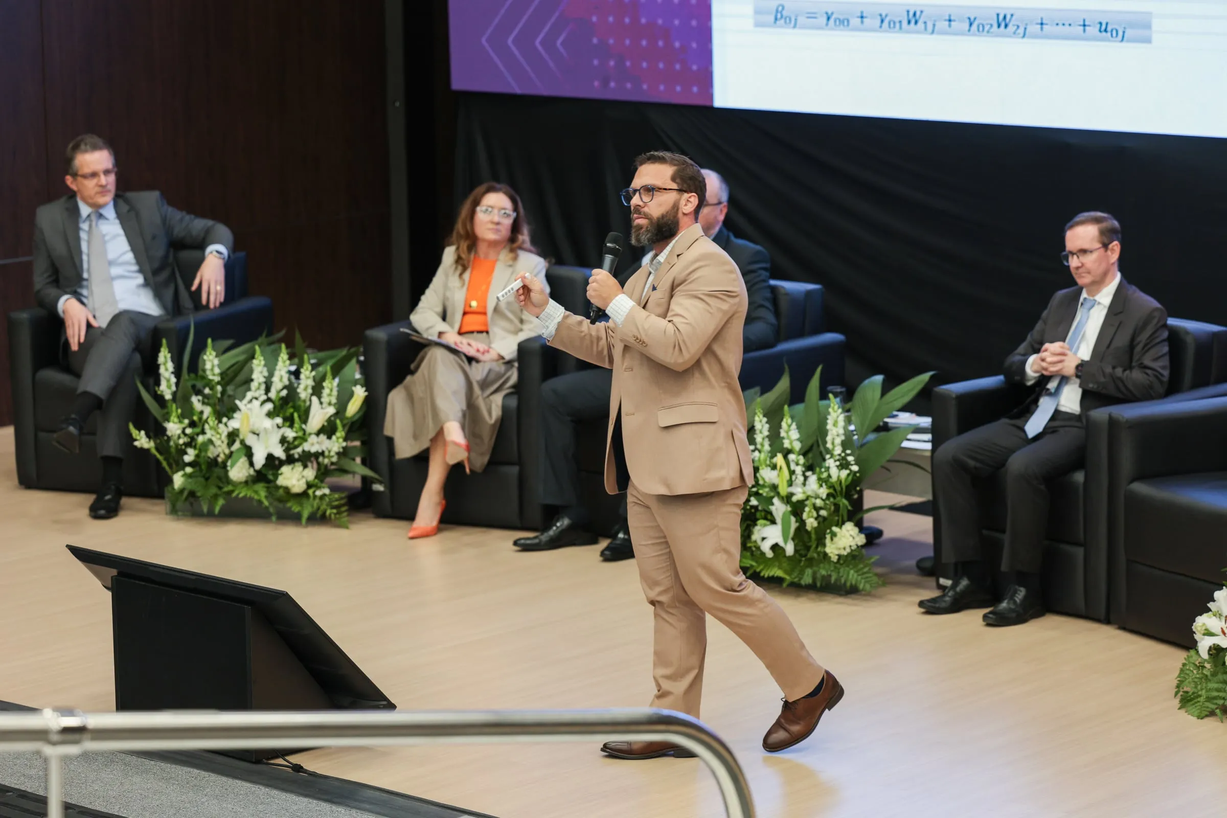 Filipe Ivo fala ao microfone no palco da Jornada Data-Driven do TJSC, com a mesa de autoridades ao fundo e uma equação estatística no telão