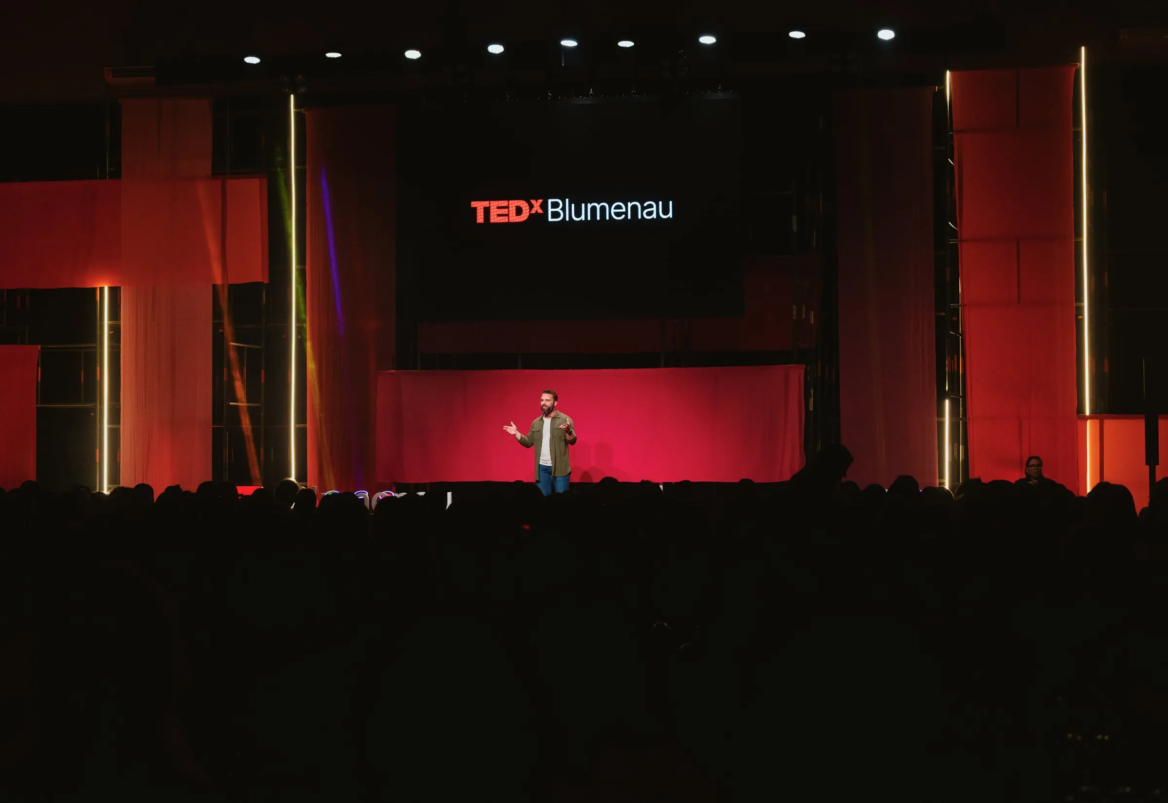 Filipe Ivo no palco vermelho do TEDxBlumenau, diante da plateia